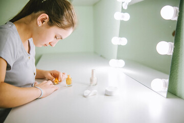 Fototapeta na wymiar Chica pintándose las uñas en su habitación, frente a su espejo de luces.