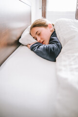 Chica dormida en su habitación con pijama oscuro y ropa de cama blanca.