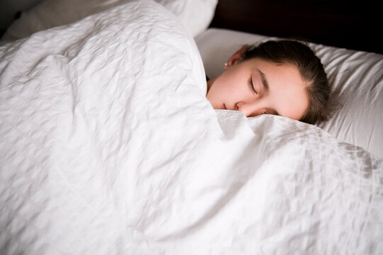 Chica dormida en una cama de colcha blanca.