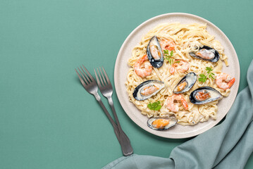Fettuccine pasta in a creamy sauce with seafood in a plate. Green pastel background. Pasta with prawns and mussels. Top view, flat lay.