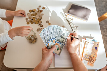 Senior woman hands together with little child counting money americain dollars and euro at home...