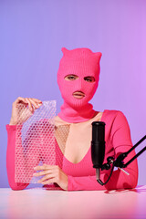 Unrecognizable young female influencer wearing pink sweater and balaclava holding bubble wrap prepared for ASMR content