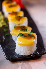 rolls with yellow sauce on top on a black plate close-up