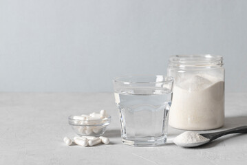 Collagen powder in spoon, glass of water, collagen capsules and jar of powder on light blue background. Healthy anti-aging concept