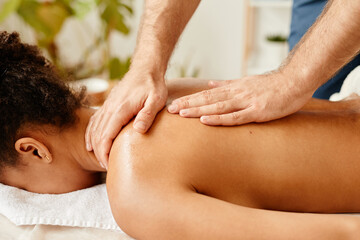 Close up of African American young woman lying on spa bed enjoying back massage, copy space