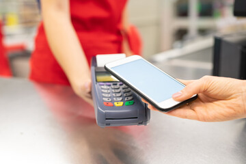 High angle close-up shot of unrecognizable young woman using online banking technology on smartphone to pay for goods in store