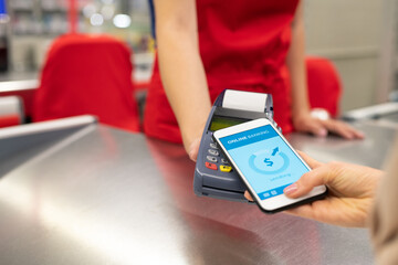 High angle close-up shot of unrecognizable young woman using online banking technology on smartphone to pay for goods in store
