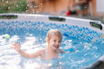 Sweet 3 years old girl enjoys summer time in swimming pool at the backyard of her home, stay home vacation concept