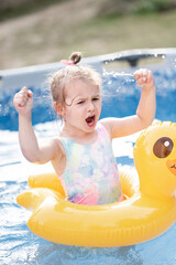 Sweet 3 years old girl enjoys summer time in swimming pool at the backyard of her home, stay home vacation concept
