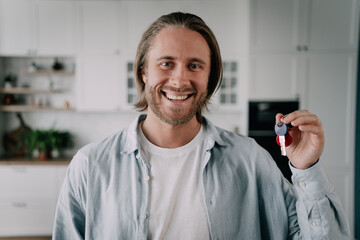 A male realtor showing the key and looking at a camera with a smile attracting customers with a good offer.