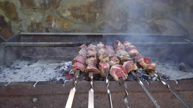 Pickled kebab is grilled on coals. Man's hand stirs skewer. Delicious pieces of marinated meat, strung on skewers, cooked on charcoal grills in fragrant hot smoke.