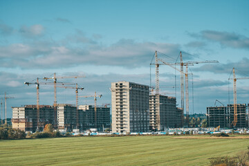 Building site with industrial construction cranes, multi-storey houses. New city districts and large green field. Blue sky with clouds. Project of urban area.