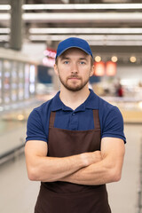 Horizontal medium portrait of modern young man wearing uniform working in store standing with arms crossed looking at camera