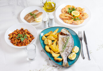 Traditional  Greek food, Dorada fish with Greek salad, Mediterranean traditional menu, Grilled sea bream, shrimps, zucchini, variety of seafood, mussels, tzatziki, potatoes, feta and ouzo