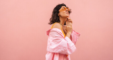 Cute caucasian young brunette woman with short haircut poses against pink background. Model wears casual summer clothes and sunglasses. Lifestyle concept 