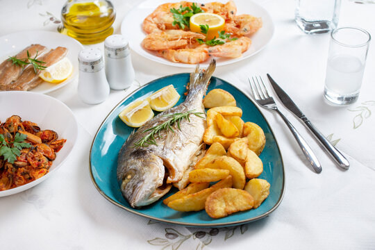 Traditional  Greek food, Dorada fish with Greek salad, Mediterranean traditional menu, Grilled sea bream, shrimps or prawns  zucchini, variety of seafood, mussels, tzatziki, potatoes, feta and ouzo