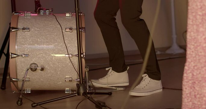 The musician's foot uses the drum pedal while making music. Make a bass rhythm. Glare on the surface of the lacquer of a musical instrument. White shoes.