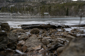 Low view of the house across the river, dry branches and stones in the foreground