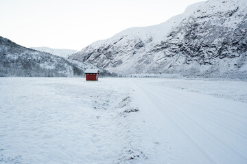 snowy norwegian mountains with a small red house in the distance to which the road leads