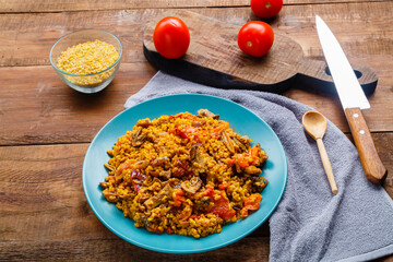 A large dish of bulgur with vegetables and mushrooms in spices on a table on a blue napkin
