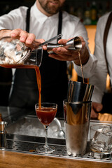 close-up on shaker cups and a wineglass into which hands of different bartenders pour drinks