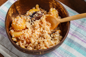 a plate of couscous with dried fruits and nuts on a wooden table on a napkin with a wooden spoon.