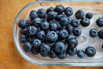 Fresh blueberries in a transparent plate on a wooden table. Top view, natural vitamins.