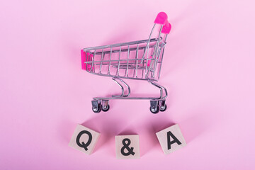 Q and A alphabet on wooden cube with trolley on pink background. Question and answer meaning...