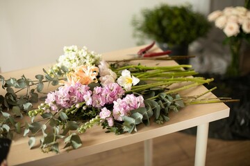 Fresh flowers, leaves, and tools to create a bouquet on a table, florist's workplace.