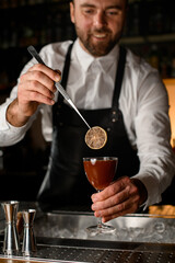 bartender holds wineglass with cocktail and garnishes it with a slice of dry lemon