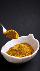 turmeric powder in a spoon and saucer on a black background