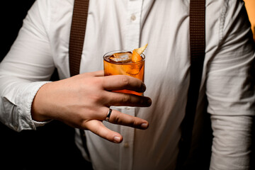 male hand accurate holds glass with cold alcoholic drink with orange zest
