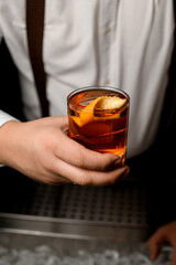 Close-up of transparent glass with cold alcoholic drink with orange zest in male hand