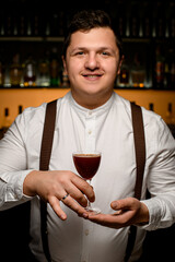smiling man bartender serving alcoholic cocktail in wineglass on the blurred bar background