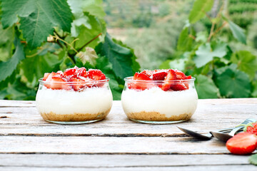 Strawberry desserts with fresh strawberries, cream cheese or natural yoghurt and oat granola in glass jars on wooden table. Delicious healthy organic summer snack or breakfast.
