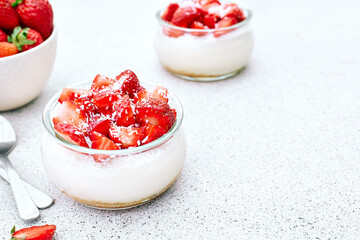 Strawberry desserts with fresh strawberries, cream cheese or natural yoghurt and oat granola in glass jars on light surface. Delicious healthy organic summer snack or breakfast.