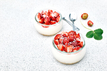 Strawberry desserts with fresh strawberries, cream cheese or natural yoghurt and oat granola in glass jars on light surface top view. Delicious healthy organic summer snack or breakfast