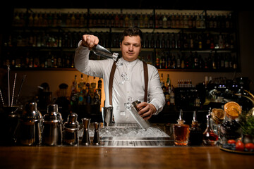great view of professional bartender skillfully pouring ice cubes from scoop into shaker cup