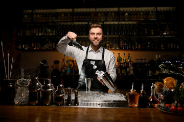 smiling man bartender skillfully pouring ice cubes from scoop into shaker cup
