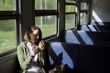 Brunette woman sitting in empty train wagon, using mobile phone. Deep shadows from the window.