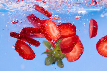 Sliced Strawberry in water with water splash and air bubbles on blue background. Close up image.