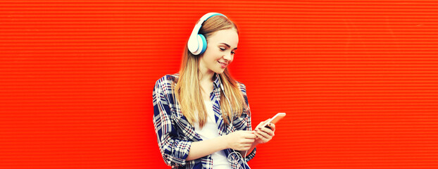 Portrait of happy woman with smartphone in wireless headphones listening to music on red...