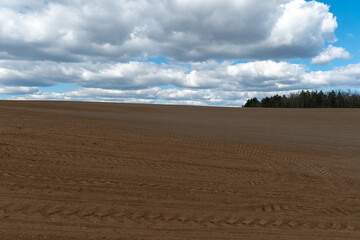 Fototapeta na wymiar Rows of soil before planting. Drawing of furrows on a plowed field prepared for spring sowing of agricultural crops. View of the land prepared for planting and growing crops.
