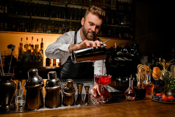 charming view of the bar counter with a variety of bar equipment and goblet in which bartender pours a cocktail