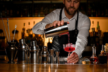 beautiful view of the bar counter with a variety of bar equipment and goblet in which bartender pours a cocktail