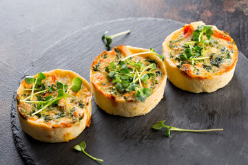 Savoury mini quiches with custard and watercress on a black round wooden board - obrazy, fototapety, plakaty