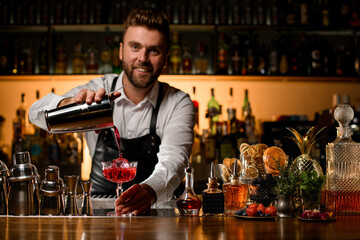 awesome beautiful view of the bar counter with a variety of bar equipment and goblet in which bartender pours a cocktail