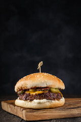 Tasty grilled beef burger with juicy meat patty, melted cheese and pickled cucumbers on the skewer