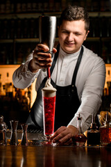 male bartender decorates glass of alcoholic cocktail with whipped cream