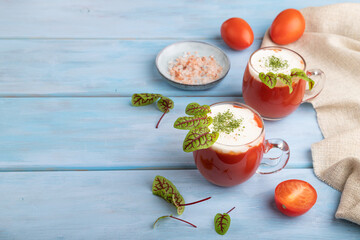 Tomato juice with sorrel, salt and sour cream in glass on blue wooden background. Side view, copy space.